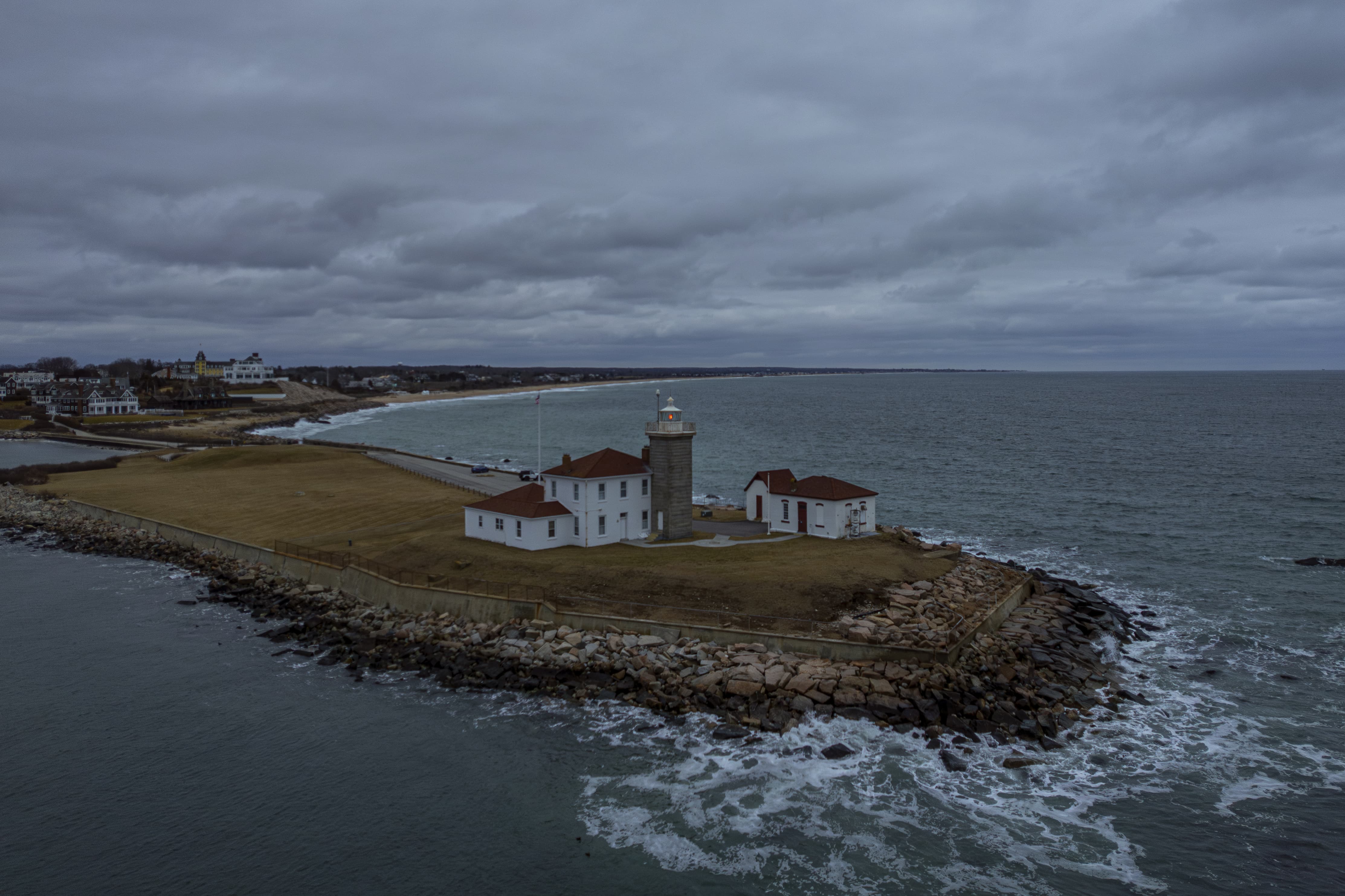A lighthouse at right by the ocean on a cloudy  day.